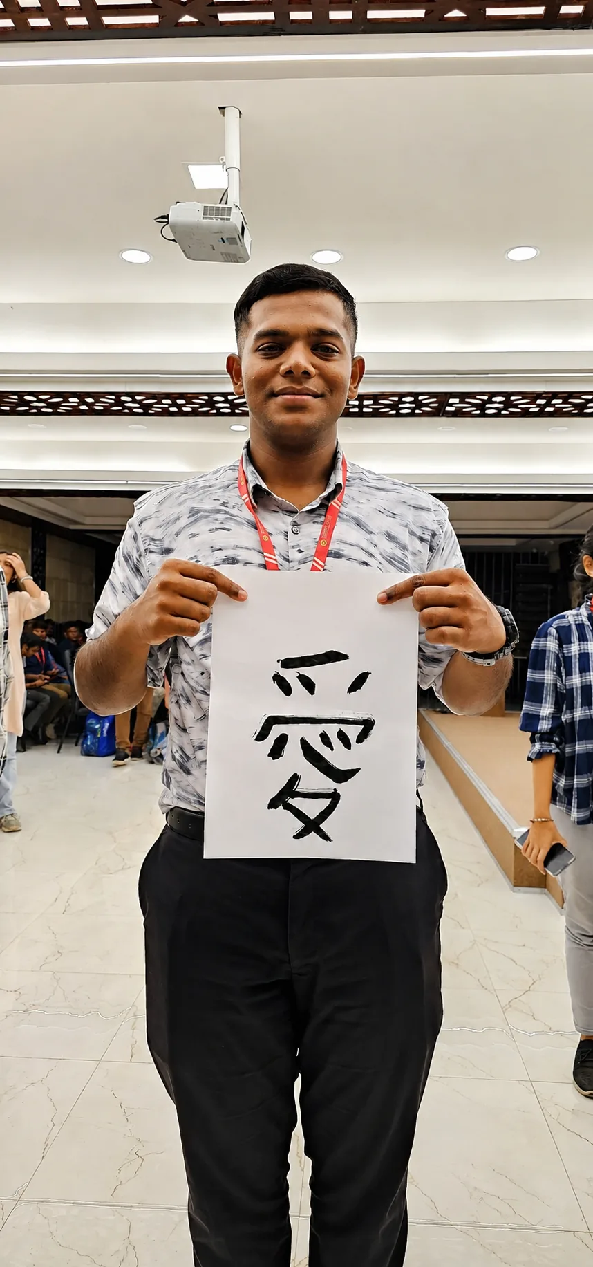 A student proudly displays his brush-written 愛 (ai, “love”)